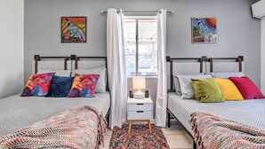 A bedroom with two beds, a nightstand with a lamp, and two wall-mounted paintings.