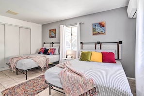 A bedroom with two beds, a large window, and artwork on the walls. - Cali Desert Oasis w/ Hot Tub + Mtn Views! (Twentynine Palms)