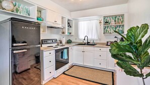 A modern kitchen with white cabinetry, a black refrigerator, and a large plant.
