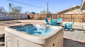 A hot tub in a backyard with a wooden fence, a table, and blue chairs.