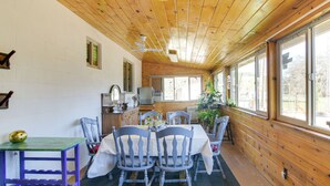 Una habitación con paneles de madera, una mesa de comedor con sillas, una pequeña cocina y ventanas amplias.
