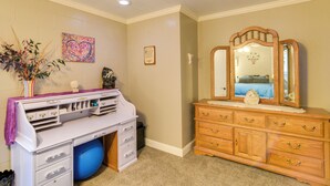 Un dormitorio con un aparador blanco, una tocador con espejo, un escritorio con cajones, una pelota de ejercicio azul y una planta decorativa.