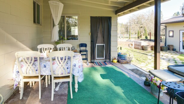 Un patio techado con una mesa y sillas, césped artificial verde y vista al jardín trasero.
