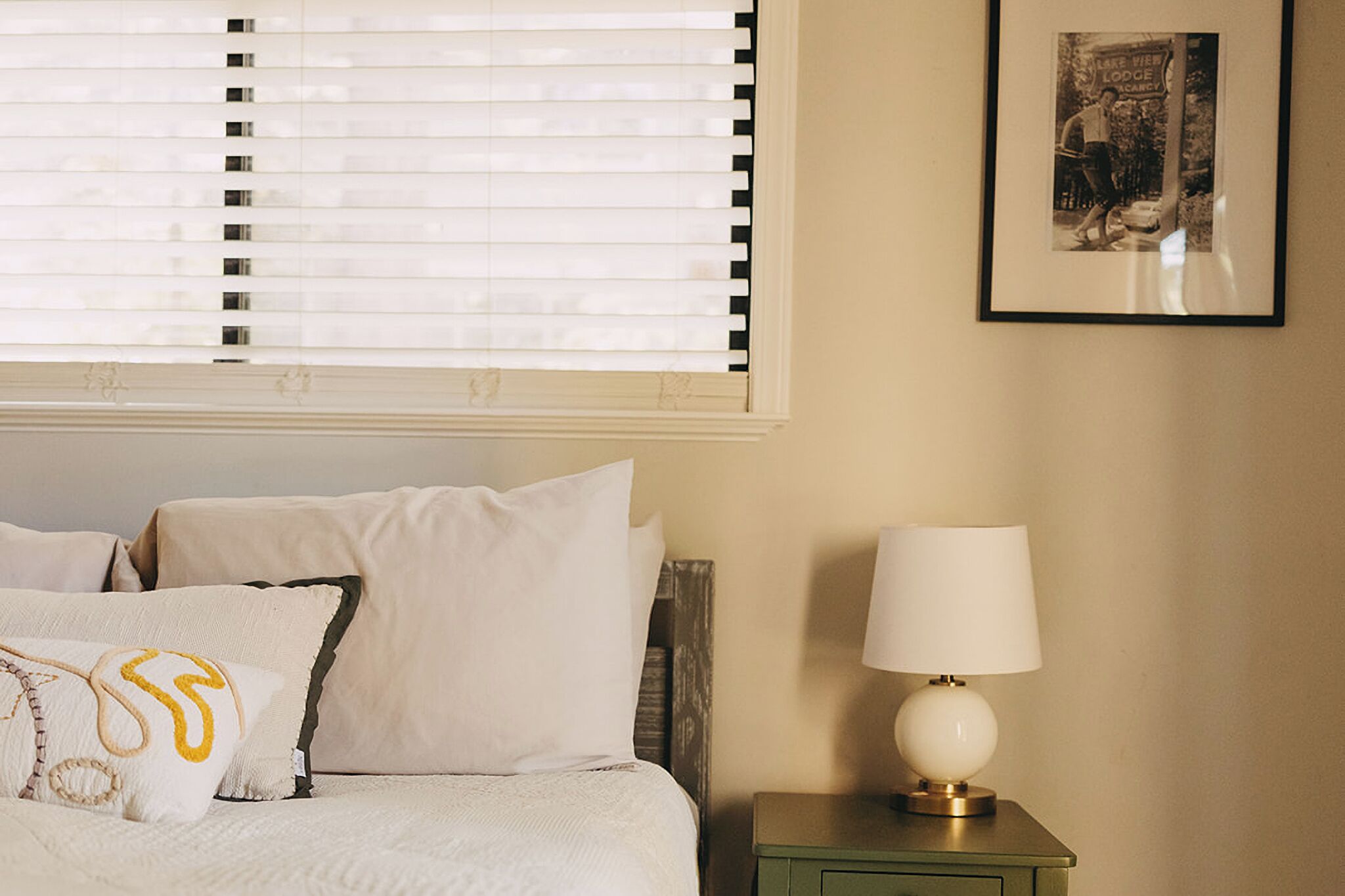 A bedroom with a bed, pillows, a nightstand, a lamp, and a framed picture on the wall.