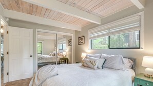 A bedroom with a large bed, a mirror, a window with blinds, and a nightstand with a lamp.