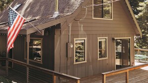 A wooden cabin with a deck, a chimney, and an American flag.