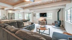 A spacious living area with a large sofa, a coffee table, and a fireplace. There is a kitchen area with cabinets and a refrigerator.