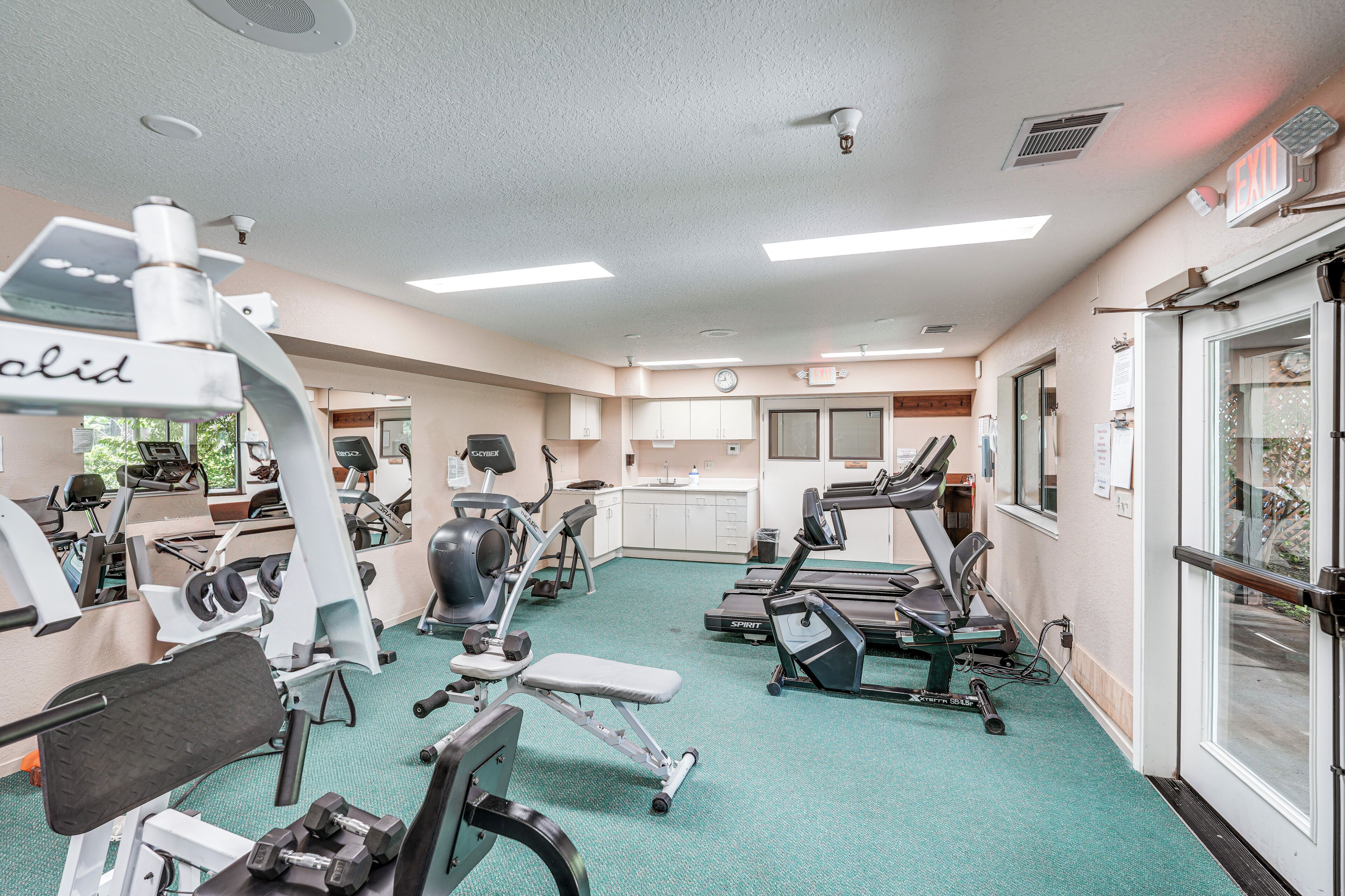 A fitness center with various exercise equipment, a reception area, and a clock on the wall.