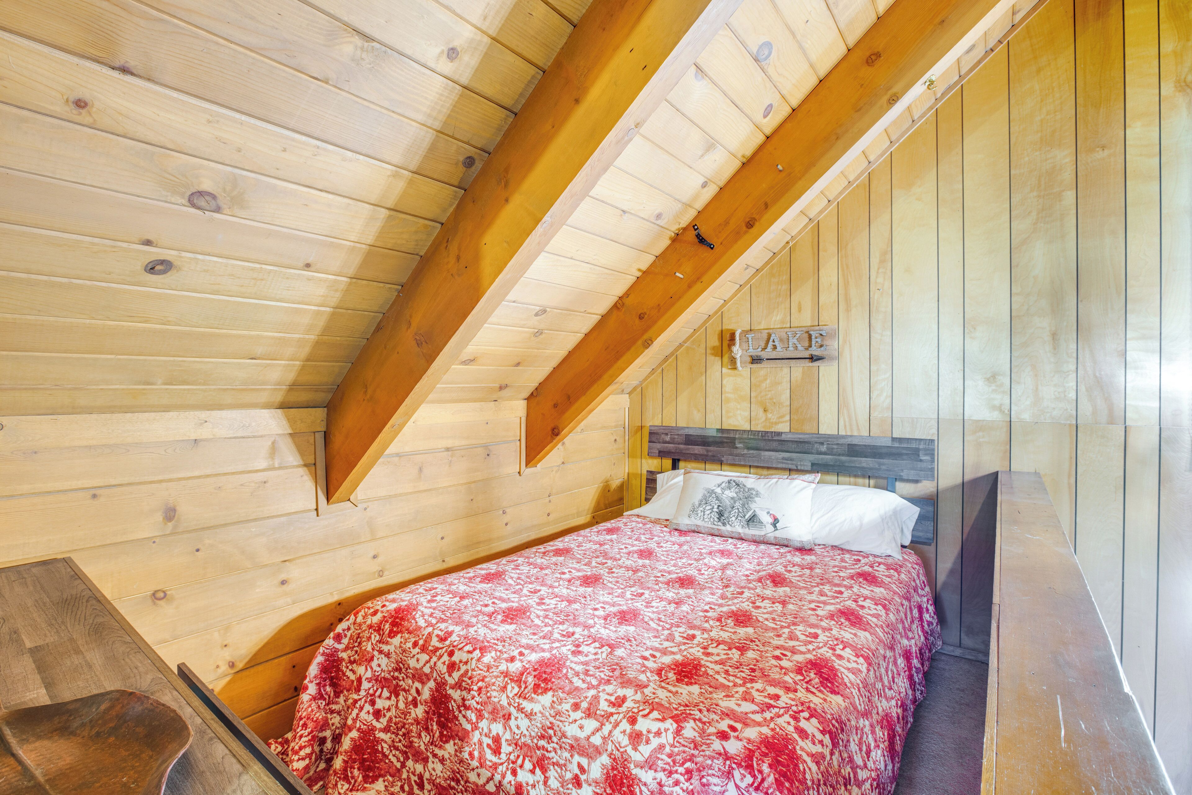 A wooden cabin bedroom with a sloped ceiling, a bed with a floral bedspread, and a wooden bench.