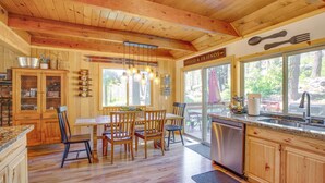 A wooden cabin kitchen with a dining area, wooden cabinets, a dishwasher, and a large window with a view of the outdoors. - 10 Mi to Ski Slopes: South Lake Tahoe Home (South Lake Tahoe)