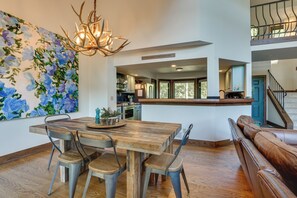 Un comedor amplio con una mesa y sillas de madera, una araña y un cuadro grande con motivos florales en la pared.