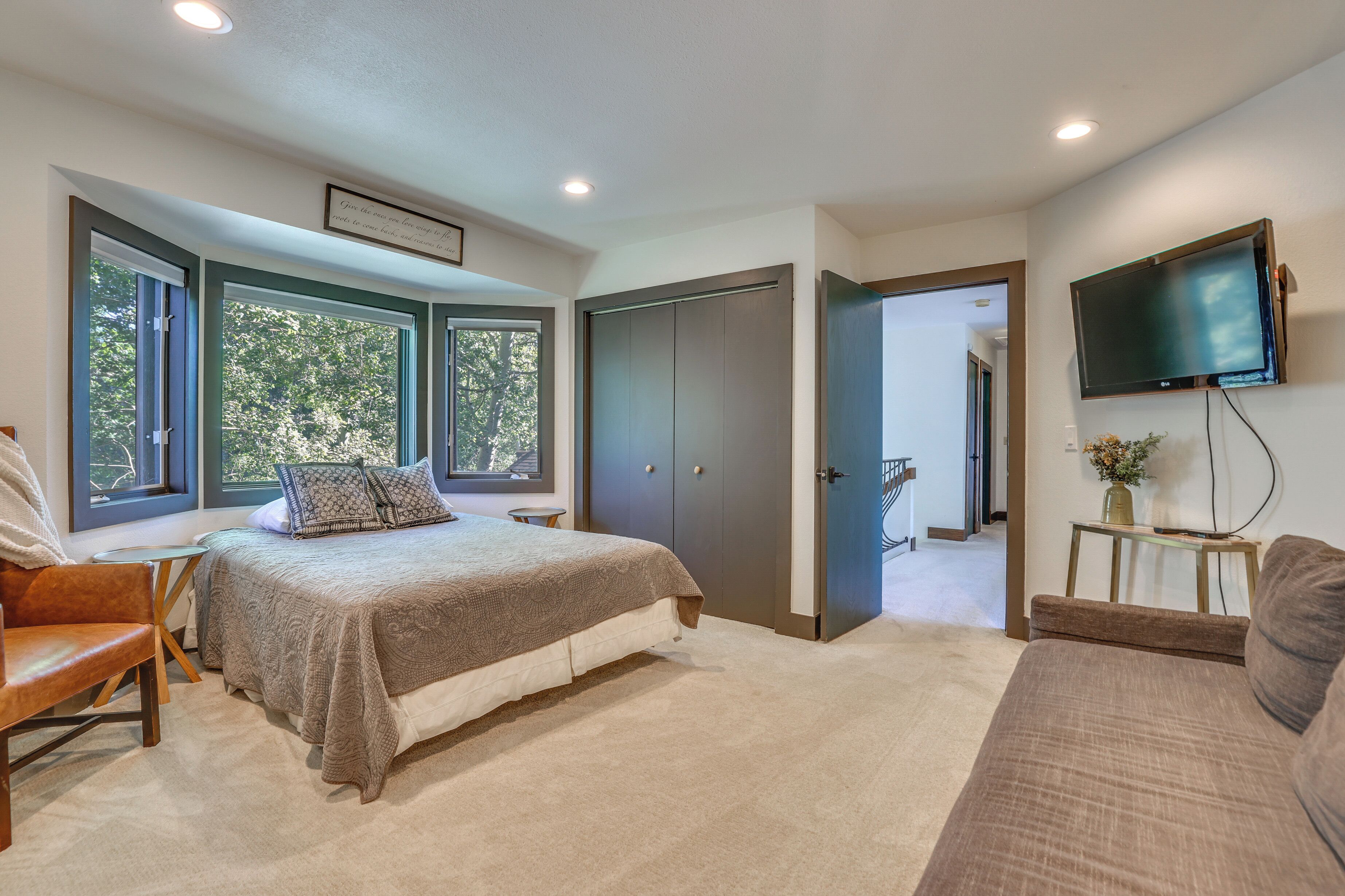 A bedroom with a bed, a chair, a TV, and large windows.