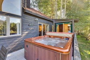 Una cabaña de madera con jacuzzi, ventanas amplias y una terraza.