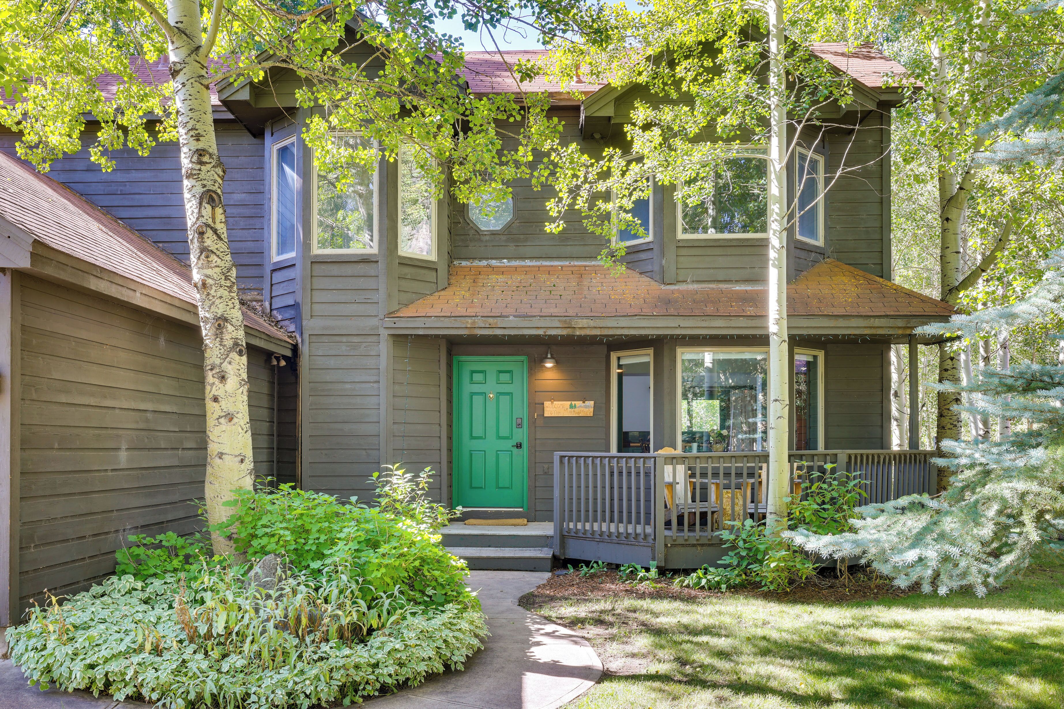 Une maison à deux étages avec une porte verte, un porche à l’avant et un petit jardin.
