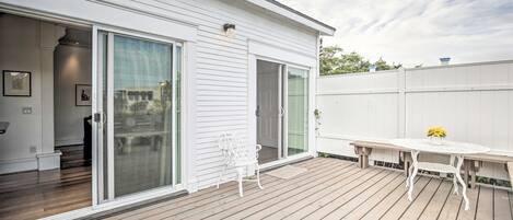 Une terrasse couverte avec une plateforme en bois, une table et une chaise blanches, et une porte-fenêtre coulissante donnant sur un espace intérieur.