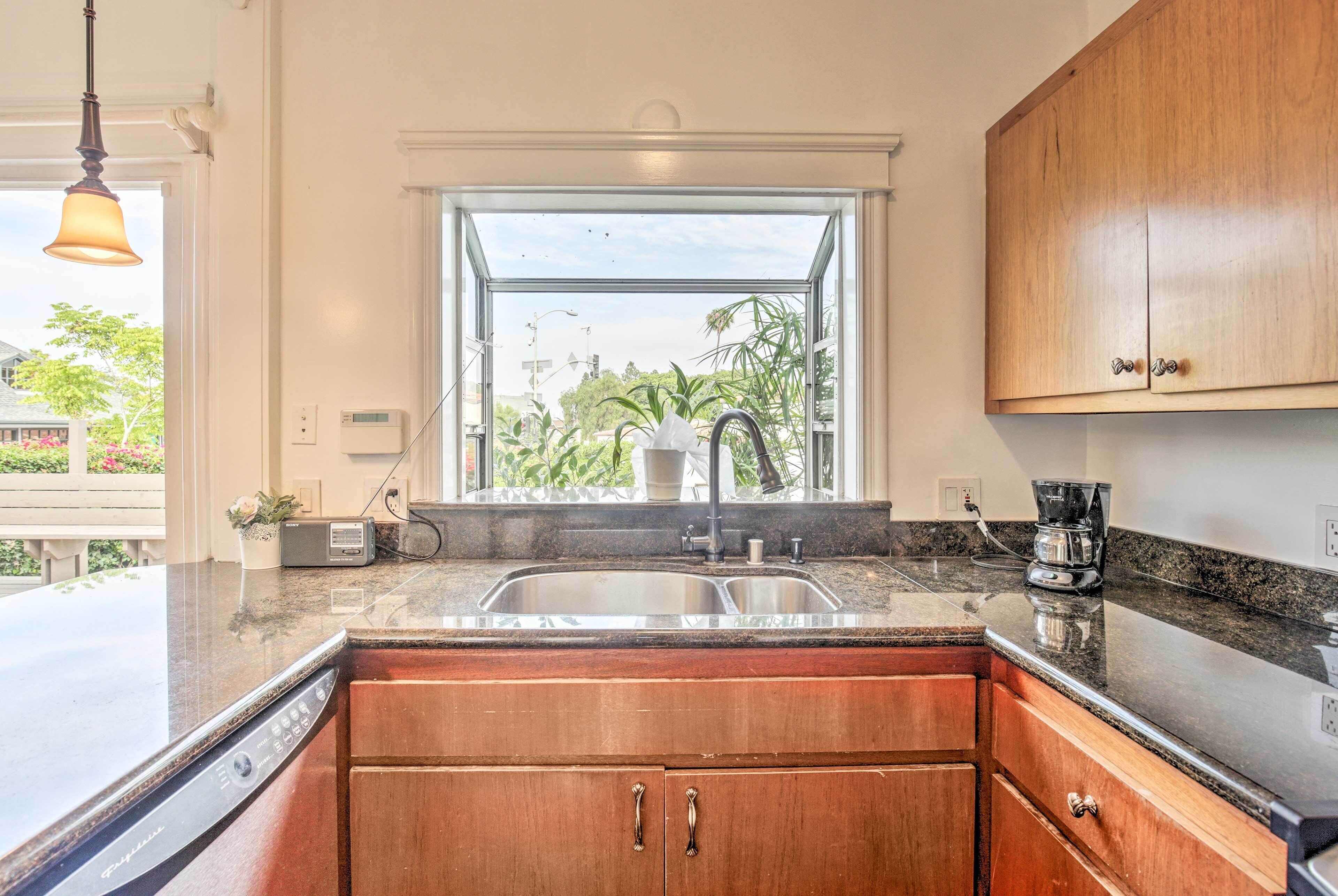 A kitchen with wooden cabinets, a double sink, and a window with a view of greenery.