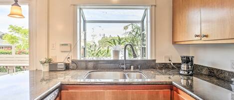 A kitchen with wooden cabinets, a double sink, and a window with a view of greenery.