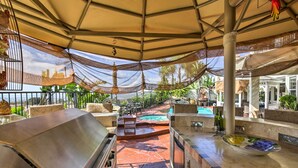 Un área de bar al aire libre con piscina, asientos cubiertos y una parrilla.