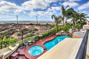 Un espace piscine offrant une vue sur un paysage désertique, entouré de palmiers et agrémenté d’une terrasse avec des chaises et une table.