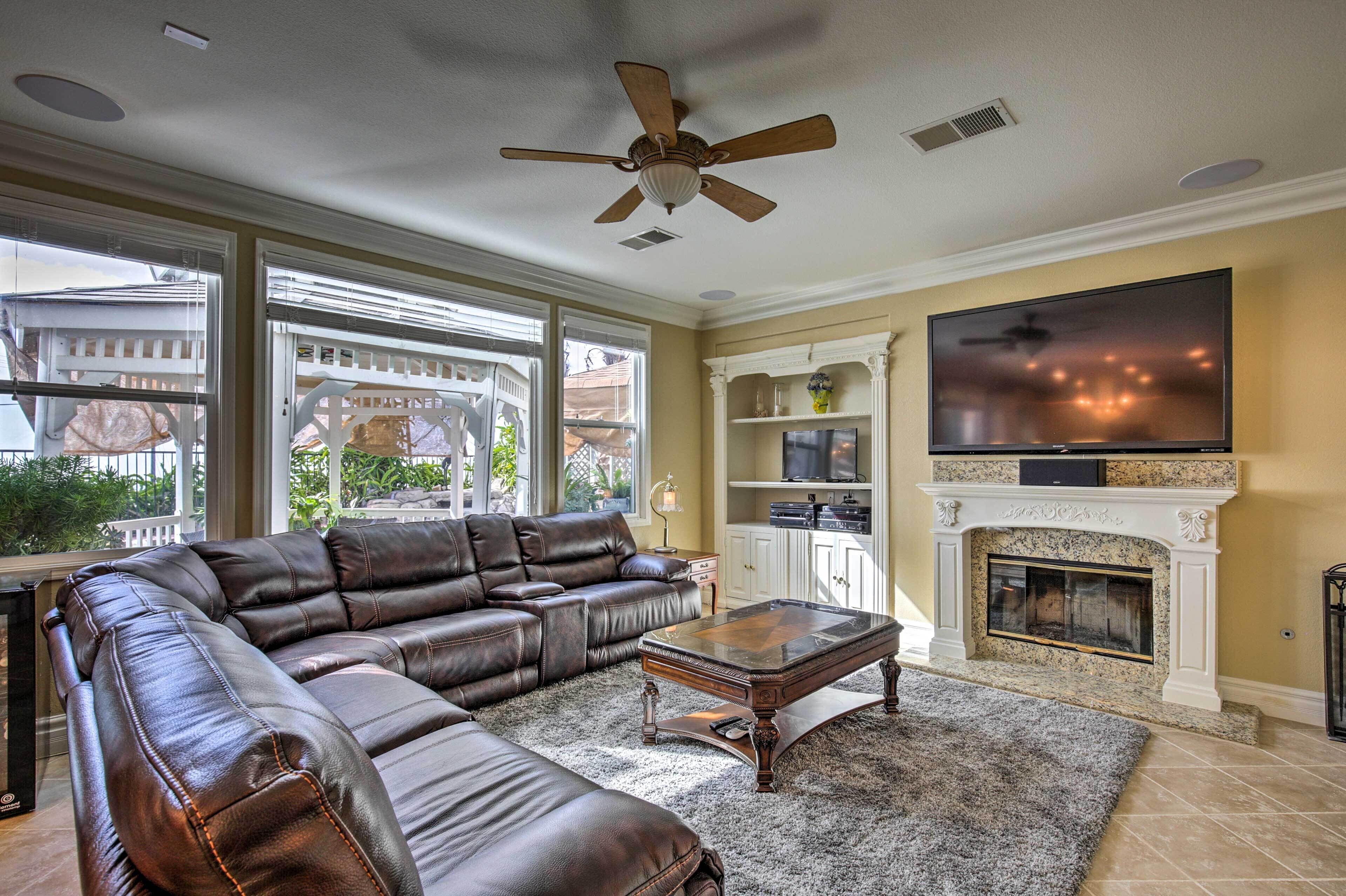 A living room with a leather sectional sofa, a coffee table, a fireplace, and a TV mounted above it.