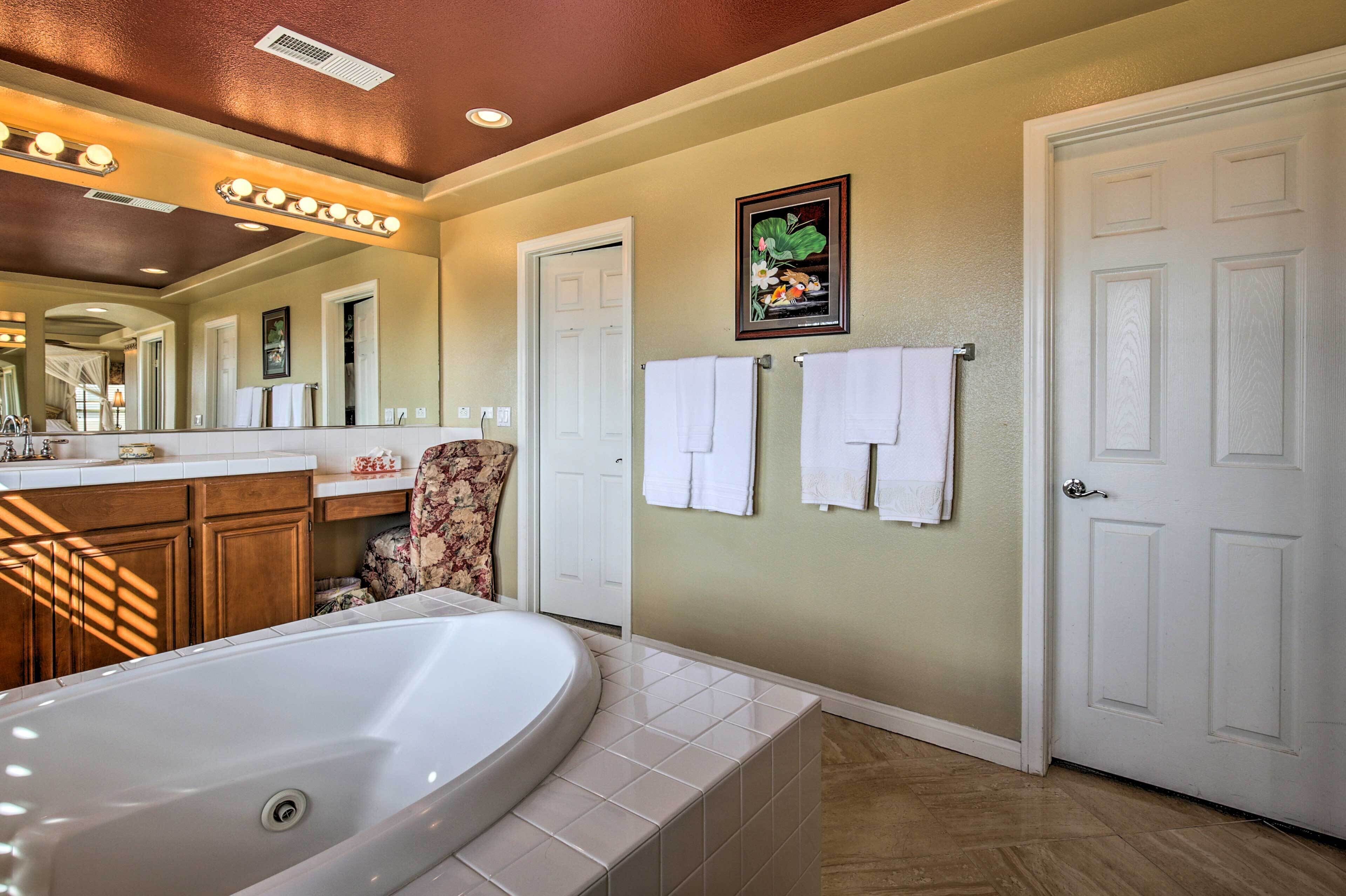 A bathroom with a large bathtub, wooden cabinets, a mirror with lights, and two white doors.