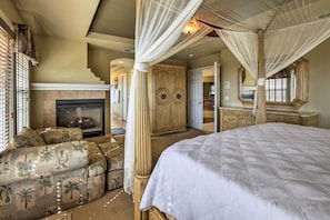 A bedroom with a large bed, a canopy bed, a fireplace, a sofa, and a wardrobe.
