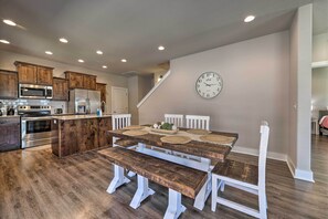 A modern kitchen with wooden cabinetry, a stainless steel refrigerator, and a dining area with a wooden table and bench. - Fayetteville House: Pool Access & Gas Grill! (Fayetteville)