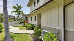 Ein Wohnhaus mit überdachter Veranda, einer geschwungenen Auffahrt und einem gepflegten Rasen mit Palmen und Sträuchern.
