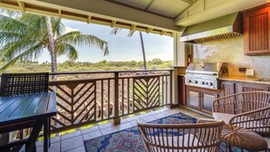 A covered outdoor area with a grill, wicker chairs, and a view of palm trees. - Luxe Maunalani Resort Condo w/ Pool + Beach Access (Kamuela)