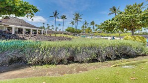 A covered outdoor area with a thatched roof, surrounded by lush greenery and palm trees. - Luxe Maunalani Resort Condo w/ Pool + Beach Access (Kamuela)