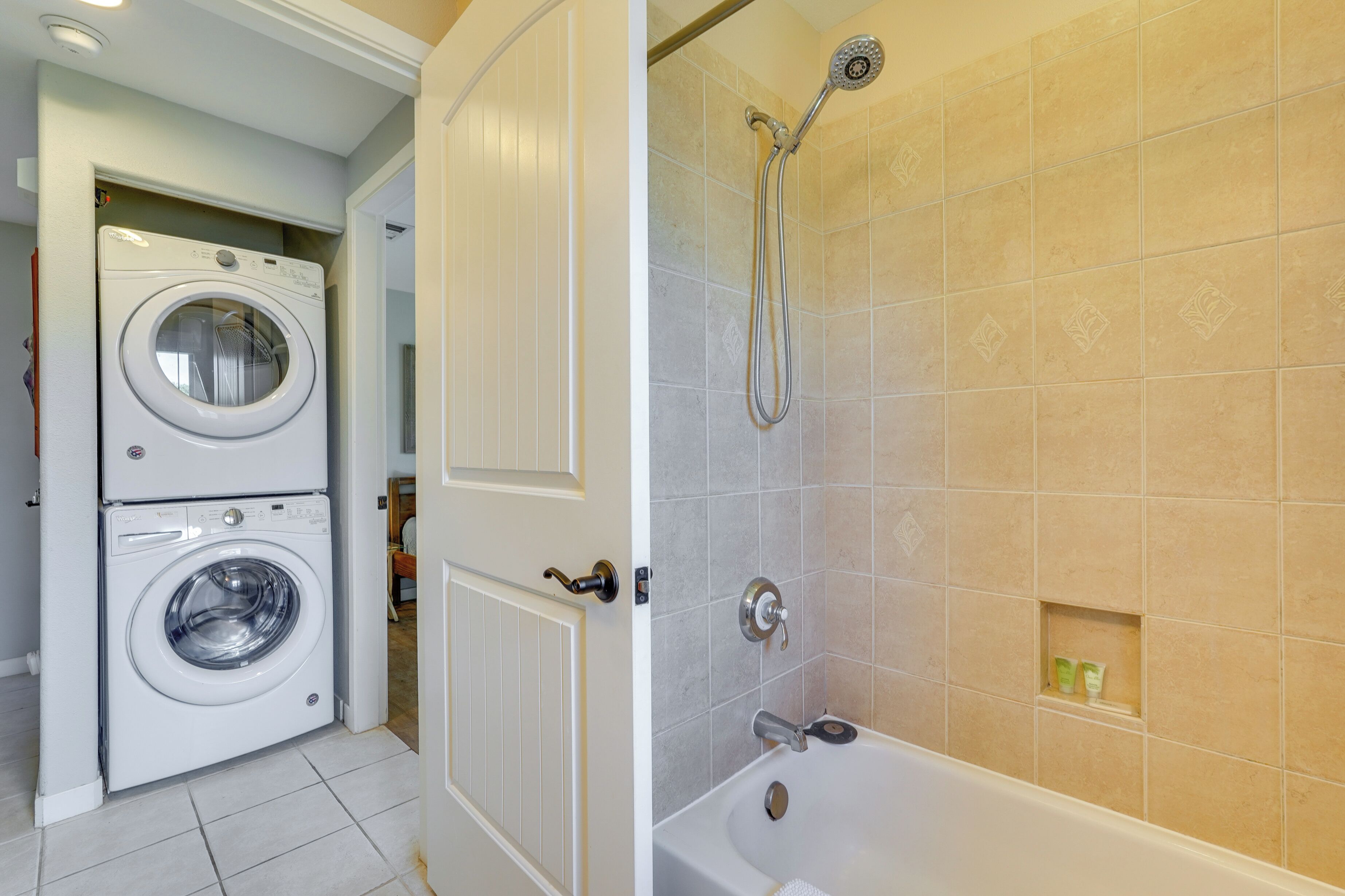 Une buanderie équipée d ’un lave-linge et d’un sèche-linge à chargement frontal, d’une douche avec un pommeau de douche amovible et d’une baignoire.