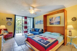 A bedroom with a bed, a ceiling fan, a window with curtains, a small table, and a wall clock. - Kailua-kona Studio - Walk to Hale Halawai Park! (Kailua-Kona)