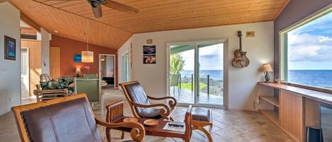 A spacious living area with wooden furniture, a ceiling fan, and a view of the ocean.