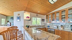 A kitchen with wooden cabinets, a marble countertop, and a dining area with wooden chairs. - Direct Oceanfront, Big Island Home (Keaau)