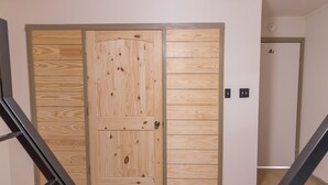 En dør af træ med et moderne design, et flisegulv og en trappe med gelænder af metal.