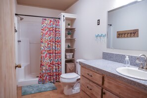A bathroom with a shower, toilet, and sink. There are shelves with plants and a mirror above the sink. - Cozy home for the smaller family (Concan)