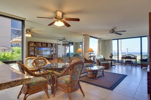 A spacious living area with a large sofa, dining table, and chairs, a television, and a balcony with a view.