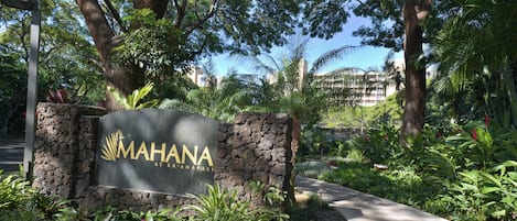 A sign for 'MAHANA at K'Anapali' with a stone wall, surrounded by lush greenery and a pathway.