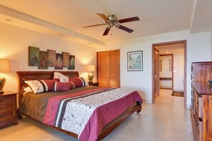 A bedroom with a bed, bedside tables, a ceiling fan, artwork on the wall, and a wooden wardrobe.