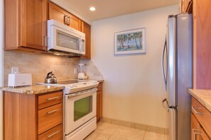 A kitchen with wooden cabinets, a microwave, an oven, a refrigerator, and a painting on the wall.