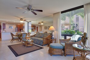 A spacious living area with wicker furniture, a large window offering a view of palm trees, and ceiling fans.