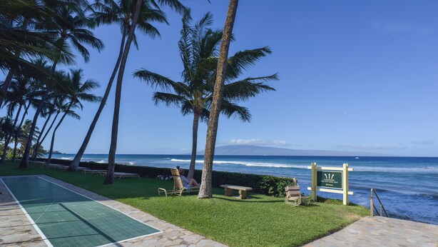 Uma área de piscina com vista para o oceano, palmeiras e um aviso.