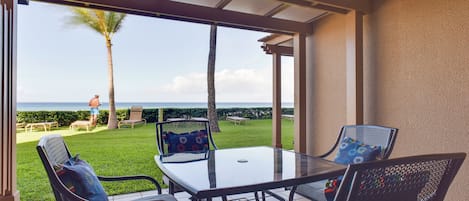 Un patio coperto con tavolo e sedie in vetro, con vista su un prato e una palma, e vista sull'oceano.