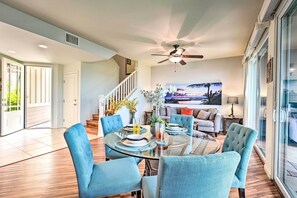 A modern living room with a glass dining table, blue upholstered chairs, a ceiling fan, and a large window with a view. - Lanai & Resort-style Perks! Kona Townhome (Kailua-Kona)