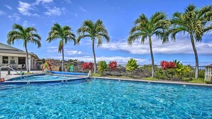 A swimming pool with clear blue water, surrounded by palm trees and red flowers. - Lanai & Resort-style Perks! Kona Townhome (Kailua-Kona)