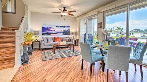 A spacious living room with a wooden floor, a ceiling fan, a sofa, a coffee table, and a view of the outdoors through large windows. - Lanai & Resort-style Perks! Kona Townhome (Kailua-Kona)