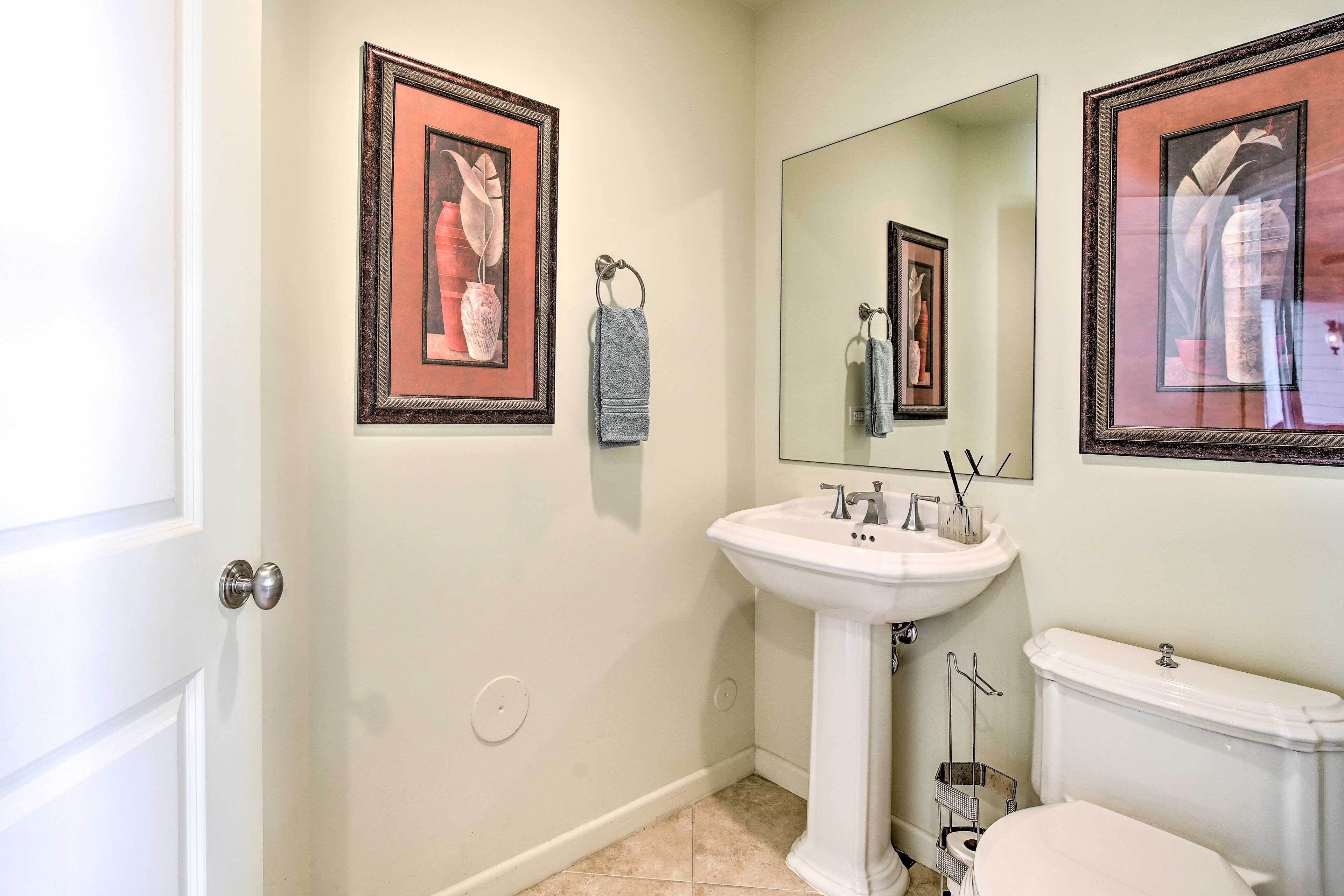 A bathroom with a white pedestal sink, a toilet, and framed artwork on the walls.