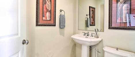 A bathroom with a white pedestal sink, a toilet, and framed artwork on the walls.