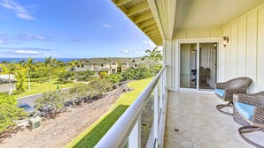 A balcony with wicker chairs, a view of a landscaped area, and a building in the background. - Lanai & Resort-style Perks! Kona Townhome (Kailua-Kona)