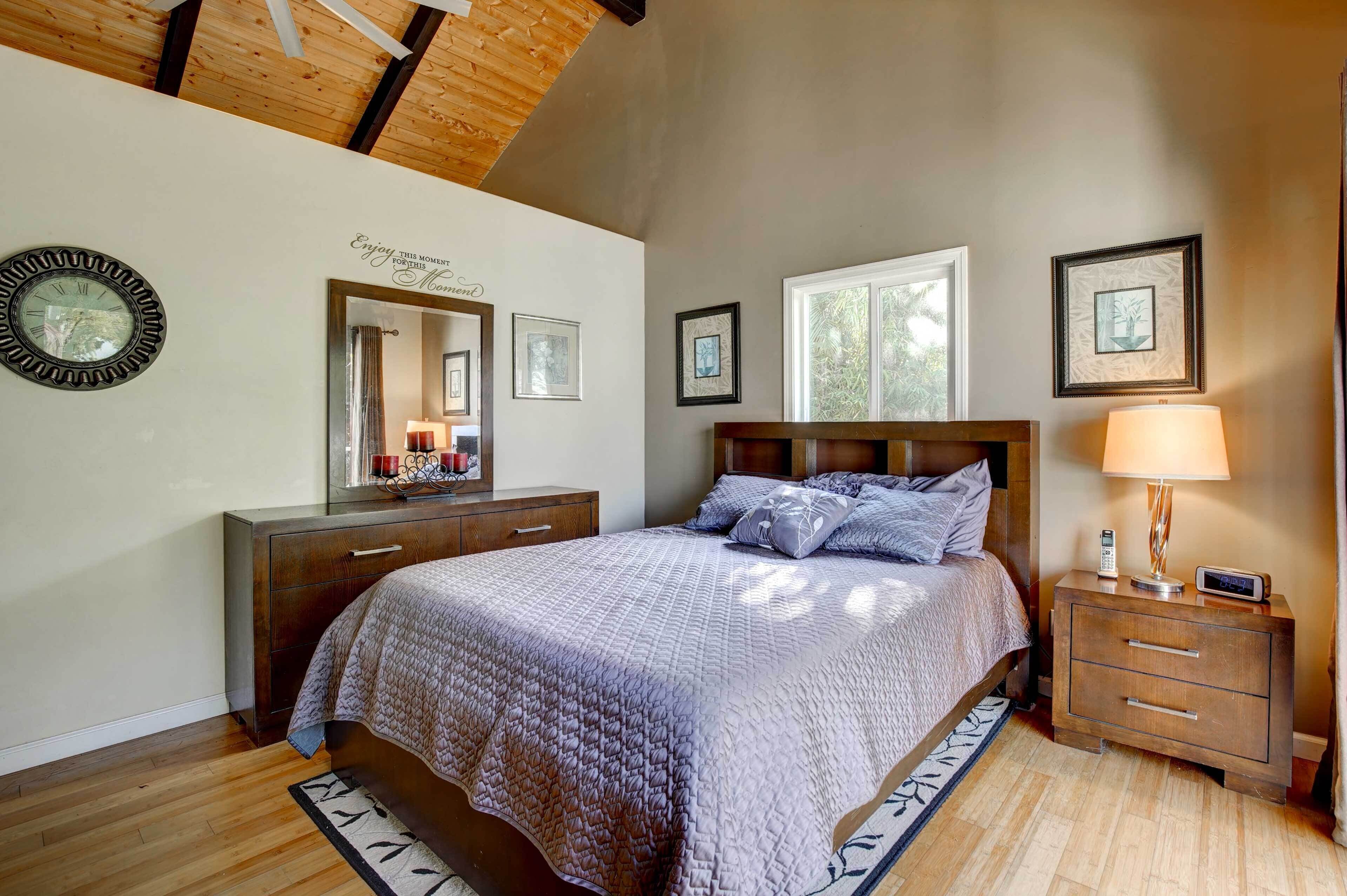 A bedroom with a bed, a nightstand, a dresser, a mirror, and framed pictures on the wall.